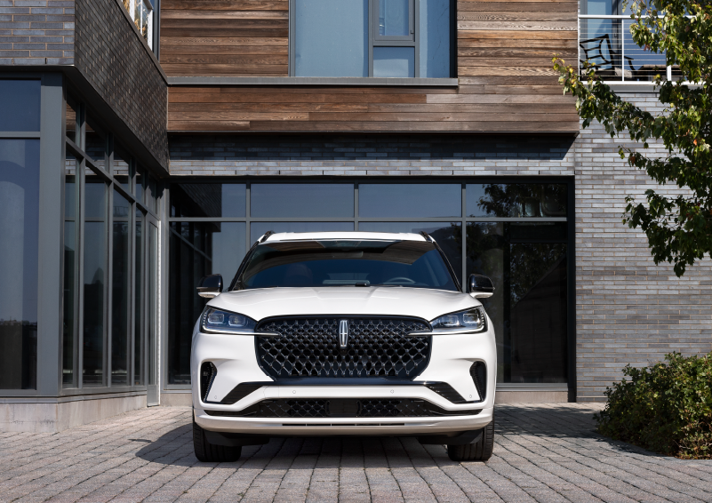 A white 2025 Lincoln Aviator® SUV is shown parked outside a modern building with gray brick and wood accents. | Joe Rizza Lincoln of Orland Park in Orland Park IL