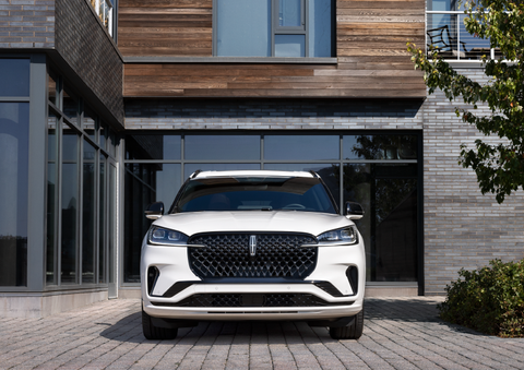 A white 2025 Lincoln Aviator® SUV is shown parked outside a modern building with gray brick and wood accents. | Joe Rizza Lincoln of Orland Park in Orland Park IL