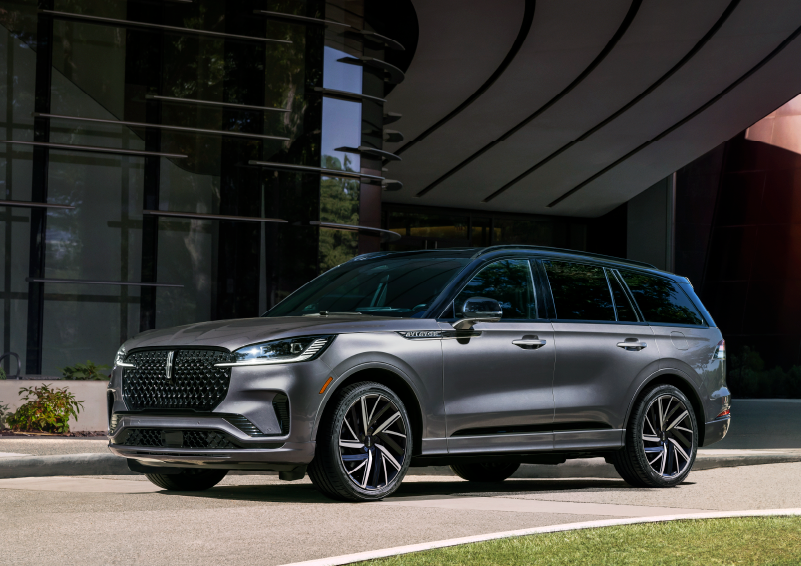 A gray 2025 Lincoln Aviator® SUV is parked outside a modern building showcasing the driver’s side of the vehicle. | Joe Rizza Lincoln of Orland Park in Orland Park IL