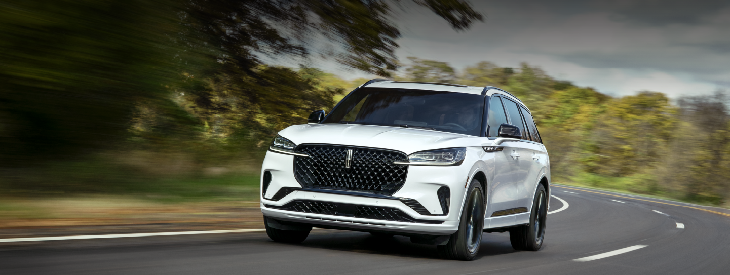 A white 2025 Lincoln Aviator® SUV is being driven down a road lined with trees. | Joe Rizza Lincoln of Orland Park in Orland Park IL