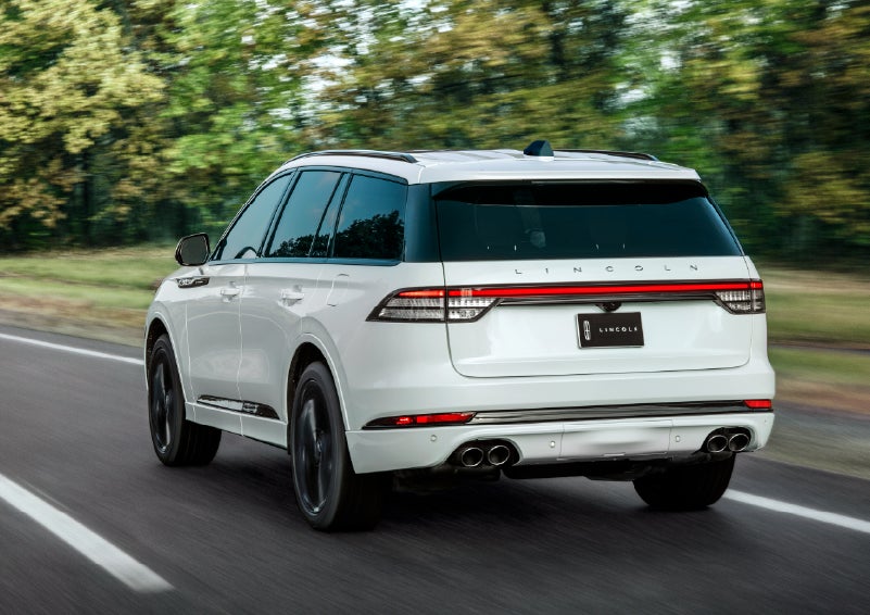 A white 2026 Lincoln Aviator® SUV is being driven away down a road lined with colorful trees. | Joe Rizza Lincoln of Orland Park in Orland Park IL
