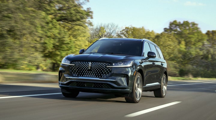 A 2026 Lincoln Black Label™ Aviator® SUV is being driven down a road lined with trees. | Joe Rizza Lincoln of Orland Park in Orland Park IL
