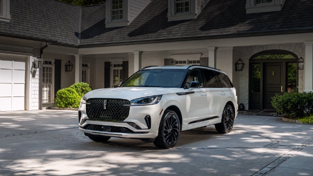 A white 2026 Lincoln Aviator® SUV is parked in the driveway of a luxury home. | Joe Rizza Lincoln of Orland Park in Orland Park IL