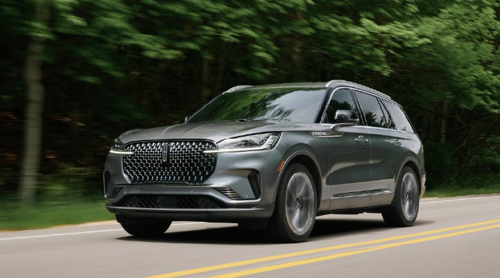 A 2027 Lincoln Aviator® SUV is being driven down a road lined with trees. | Joe Rizza Lincoln of Orland Park in Orland Park IL